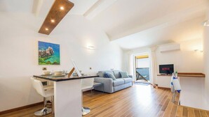 Ein modernes Wohnzimmer mit Holzboden, einem grauen Sofa, einem Esstisch mit Stühlen, einem Fernseher und einem Bild an der Wand.