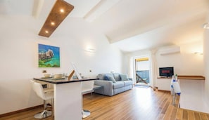 A modern living room with a wooden floor, a grey sofa, a dining table with chairs, a TV, and a painting on the wall. - “Vista Mare Genova”A two-level gem with a spectacular sea view, unique in the area.Lower floor: Bedroom with premium-quality mattress, bathroom, and a cozy corner with table and chess set overlooking the sea.Upper floor: Living room with sofa bed, fu (genova)