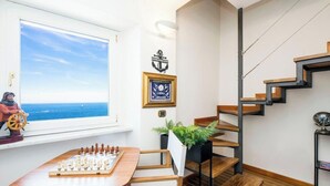 Ein Zimmer mit Schachbrett, einem Meerblick durch das Fenster, einer Treppe und einem gerahmten Zertifikat an der Wand.