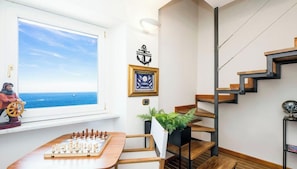 A room with a chessboard, a window with a view of the sea, a staircase, and a framed certificate on the wall. - “Vista Mare Genova”A two-level gem with a spectacular sea view, unique in the area.Lower floor: Bedroom with premium-quality mattress, bathroom, and a cozy corner with table and chess set overlooking the sea.Upper floor: Living room with sofa bed, fu (genova)