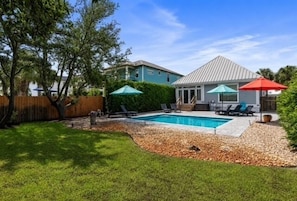 Ein Garten mit Schwimmbad, einer überdachten Terrasse und einem eingezäunten Bereich.