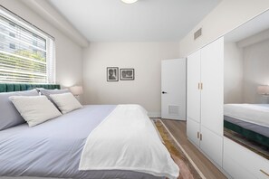 Ein Schlafzimmer mit Bett, Kleiderschrank, Nachttischen und einem Fenster mit Jalousien.