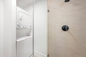 Ein modernes Badezimmer mit integrierter Waschmaschine und Trockner, einer Dusche mit schwarzem Wasserhahn und einer gefliesten Wand.