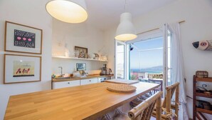 Een keuken met een houten tafel, hangende lampen en uitzicht op zee.