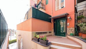 Um prédio residencial com uma porta verde, uma varanda com roupas penduradas e plantas em vasos nos degraus.