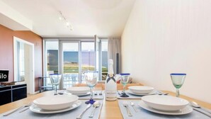 Un comedor con una mesa dispuesta para cuatro personas, una botella de vino y vistas del paisaje a través de amplias ventanas.