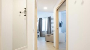 Un pasillo que conduce a una sala de estar con un sofá, un televisor y una ventana con cortinas.