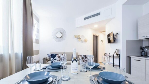 Un comedor moderno con una mesa dispuesta para cuatro, una cocina al fondo y una sala de estar con sofá.