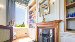 Ein Zimmer mit Kamin, einem fensterbehangenen Fenster, einem Bücherregal und einem Wandspiegel.