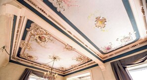 Una habitación con decoraciones ornamentales en el techo, un candelabro y una ventana con cortinas.