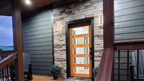 Um deck de madeira que leva a uma fachada de pedra e madeira, com uma porta de vidro.