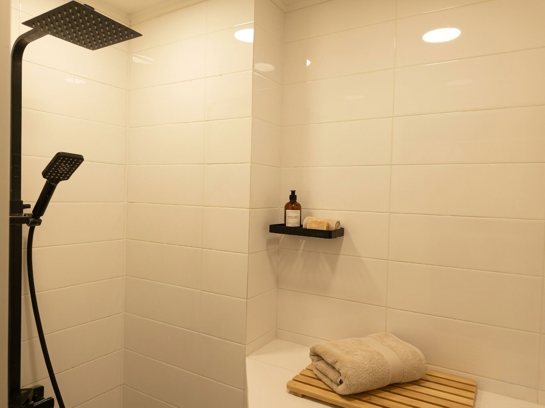 Une salle de bain avec des carreaux blancs, une pomme de douche, une serviette et une étagère contenant des articles de toilette.