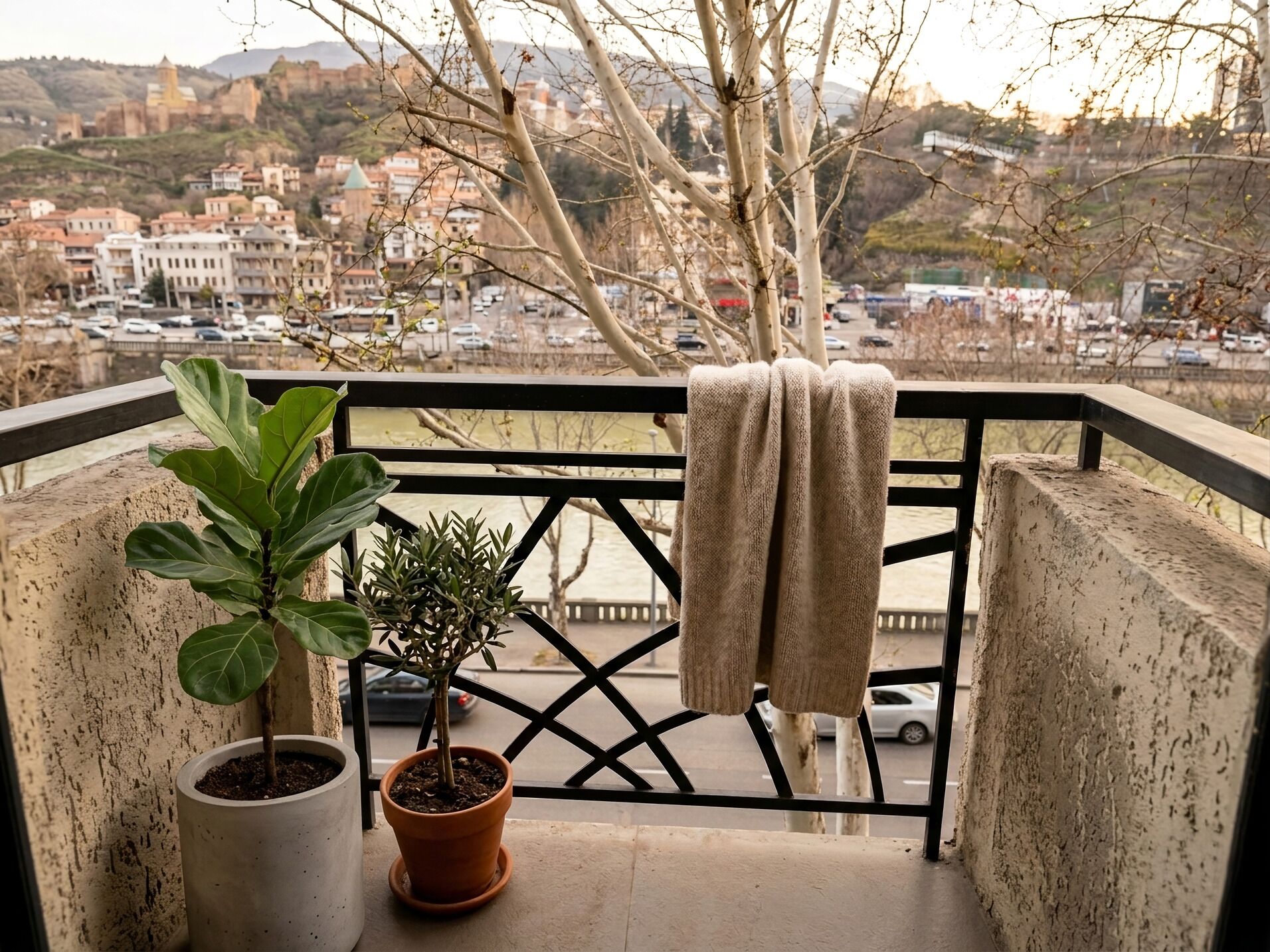 Een balkon met een bloempot, een handdoek en uitzicht op een stadsgezicht.
