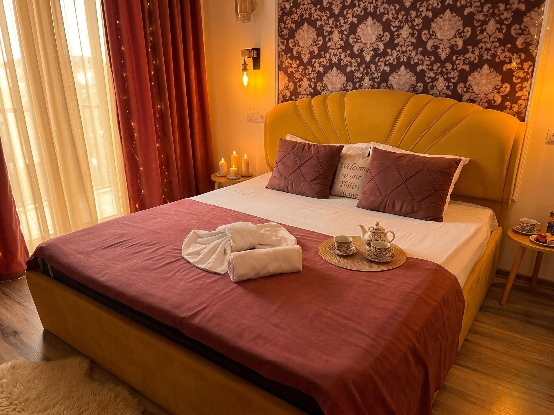 Une chambre d’hôtel avec un lit, des oreillers, une table de chevet sur laquelle se trouve un service à thé, et un mur orné d’un motif floral.