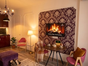 Una sala de estar acogedora con chimenea, televisor y comedor con una mesa dispuesta para tomar té.