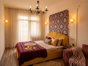 Un dormitorio con cama, candelabro, cortinas, papel tapiz estampado y apliques de pared.