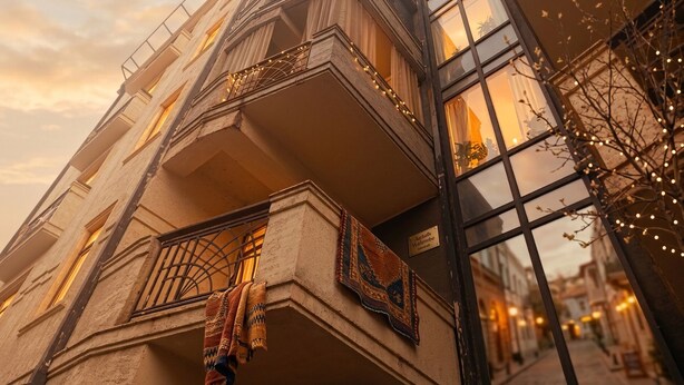 Un edificio de varios pisos con un balcón, un letrero que indica un restaurante y una vista de la calle con otros edificios.
