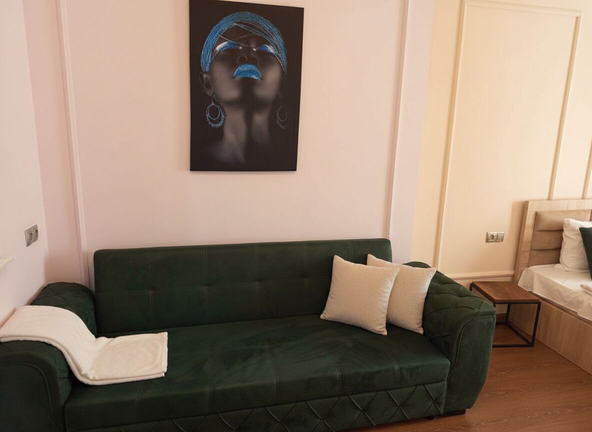 Ein grünes Sofa mit weißen Kissen, ein gerahmtes Kunstwerk darüber und ein Bett mit Holz-Kopfstück im Hintergrund.