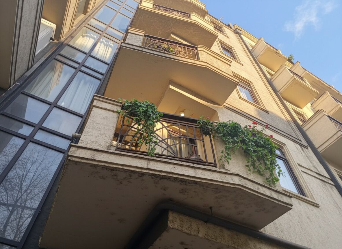 A multi-story building with balconies, large windows, and some greenery.