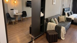 Una habitación de hotel moderna con sofá, una pequeña mesa con sillas, televisor y armario.