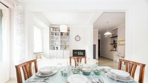 A dining area with a table set for four, a bookshelf, and a clock on the wall. - Beach 7M| 1BR| Wifi| Nervi Park By Tilo (Genova)