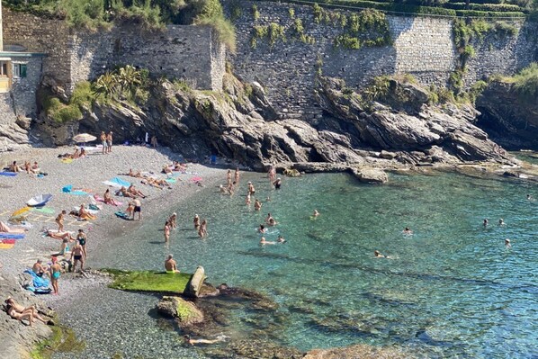 A rocky beach with clear water, people sunbathing and swimming, and a stone wall in the background. - Beach 6M| 1BR| Parking by Tilo (Genova)