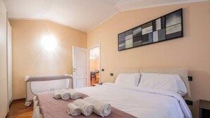 Quarto de hotel com cama, mesa de cabeceira, obra de arte na parede e porta para o banheiro.