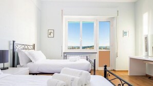 Quarto de hotel com duas camas, uma escrivaninha, uma cadeira, janela com vista e radiador.