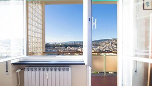 Quarto com uma janela ampla que dá para a paisagem urbana, um radiador e uma porta com maçaneta.