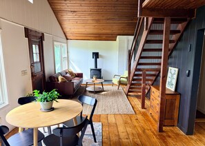 Una sala de estar acogedora con un sofá, una mesa con sillas, una escalera y una chimenea.