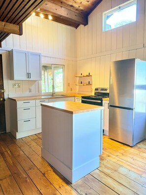 Eine Küche mit weißen Schränken, einem Edelstahlkühlschrank, Holzboden und einem Fenster.