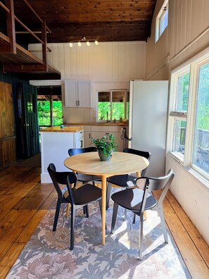 Ein Holzinterieur mit einem runden Tisch, Stühlen, einem Kühlschrank und einem Fenster mit Blick auf Grünflächen.