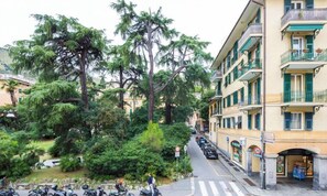 Straßenansicht mit abgestellten Rollern, einer Fußgängerampel und einem Gebäude mit Balkonen und einem Laden Eingang.