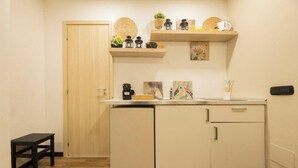Une cuisine compacte avec une porte en bois, une petite table et un plan de travail sur lequel se trouvent une machine à café et quelques objets décoratifs.