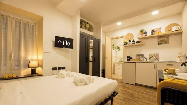 Une chambre d’hôtel comprenant un lit, un bureau avec une lampe, une kitchenette et une salle de bain.