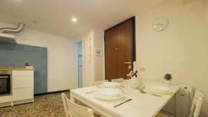 A dining area with a table set for two, a microwave, a small oven, and a clock on the wall. - AQUARIUM 1'|1BR|A/C| WIFI|BY TILO (Genoa)