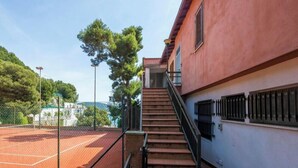 Ein Tennisplatz neben einem Gebäude mit einer Treppe, die zu einem Balkon führt.