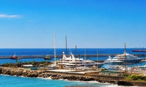 Eine Marina mit vor Anker liegenden Yachten, einem steinernen Wellenbrecher und dem Meer im Hintergrund.