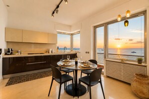 Eine moderne Küche mit Essbereich, großen Fenstern mit Sonnenuntergangsblick und einem Balkon mit Meerblick.