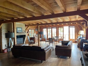 Une pièce spacieuse de style loft, avec des poutres apparentes, une cheminée, un téléviseur et un coin repas comprenant des chaises et une table.