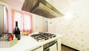 A kitchen with a gas stove, a bottle of wine, and a bag of snacks on the counter. - Ferrari | Room | Street XX | By Tilo (Genoa)