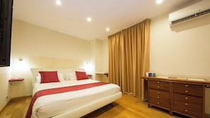 Camera d'albergo con un letto, una cassettiera in legno, un comodino e un condizionatore d'aria.
