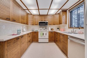 A compact kitchen with wooden cabinets, a microwave, a stove, and a sink. - Dolly - Large Home, Fast Wi-Fi, BBQ & Dbl Garage (Edmonton)