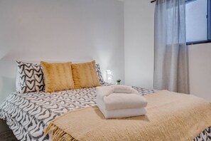 A bedroom with a bed, pillows, a bedside lamp, and a window with curtains.