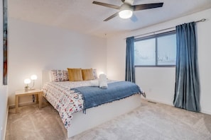 A bedroom with a bed, a nightstand, a ceiling fan, and a window with curtains.