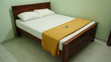 A single bed with a wooden headboard and a yellow blanket, a white pillow, and a remote control on the bed.