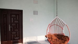 Una habitación con suelo de cuadros, un sillón colgante con cojín, una puerta de madera y un interruptor de luz en la pared.