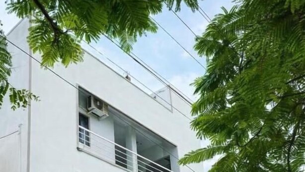 Un edificio moderno de dos pisos con techo plano, un balcón en el nivel superior y una entrada con portón.