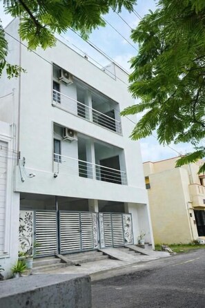 Un edificio moderno de dos pisos con techo plano, un balcón en el nivel superior y una entrada con portón.