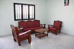 A room with a sofa, two chairs, a small table, a window with bars, and a framed picture on the wall. - Bhagawan Guest House (Tiruvannamalai)